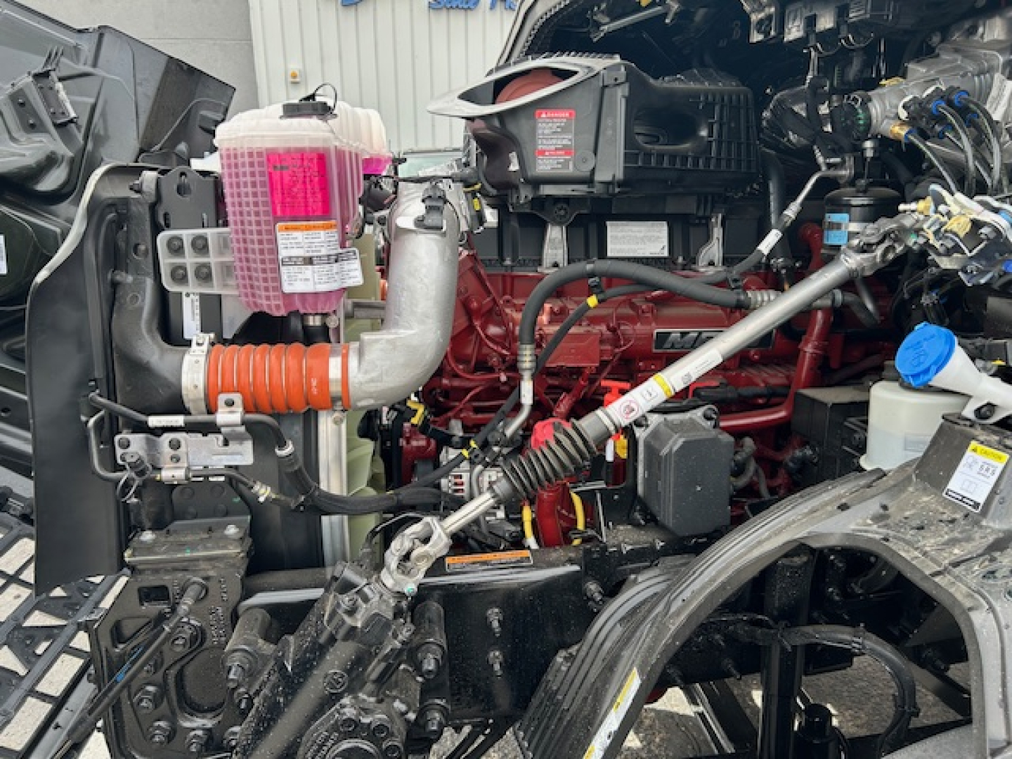Mack AN64T engine bay showing pink coolant reservoir, red diesel engine, and various hoses and wiring.