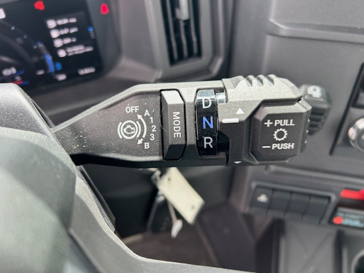 Steering column stalks of a 2027 Mack AN64T showing drive mode selector and gear shift indicator with MODE, OFF, 1-5, N, R, and push-pull controls.