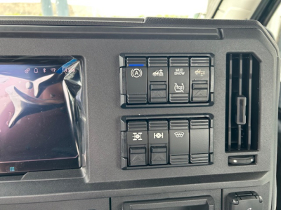 Dashboard panel of a 2027 Mack AN64T showing multiple control switches and air vents with a screen on the left.