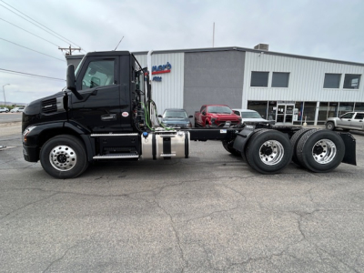 Mack AN64T conventional daycab tractor side view showing fuel tanks and dual rear axles in front of a dealership.