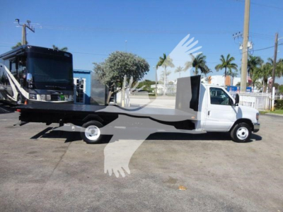 Flatbed tow truck side view showing white cab and long flatbed with wheel lifts, no visible license plate, clear blue sky.