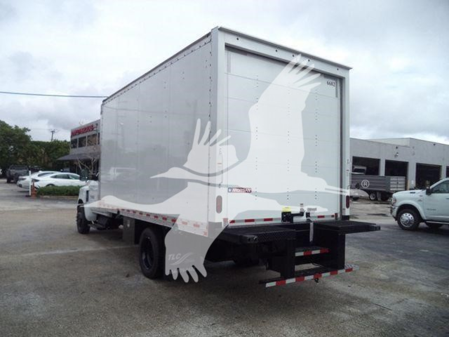 Box truck with rear cargo area showing blank white box and black bumper; no legible text visible on side; rear doors closed; some watermark graphic overlay of a bird shape.