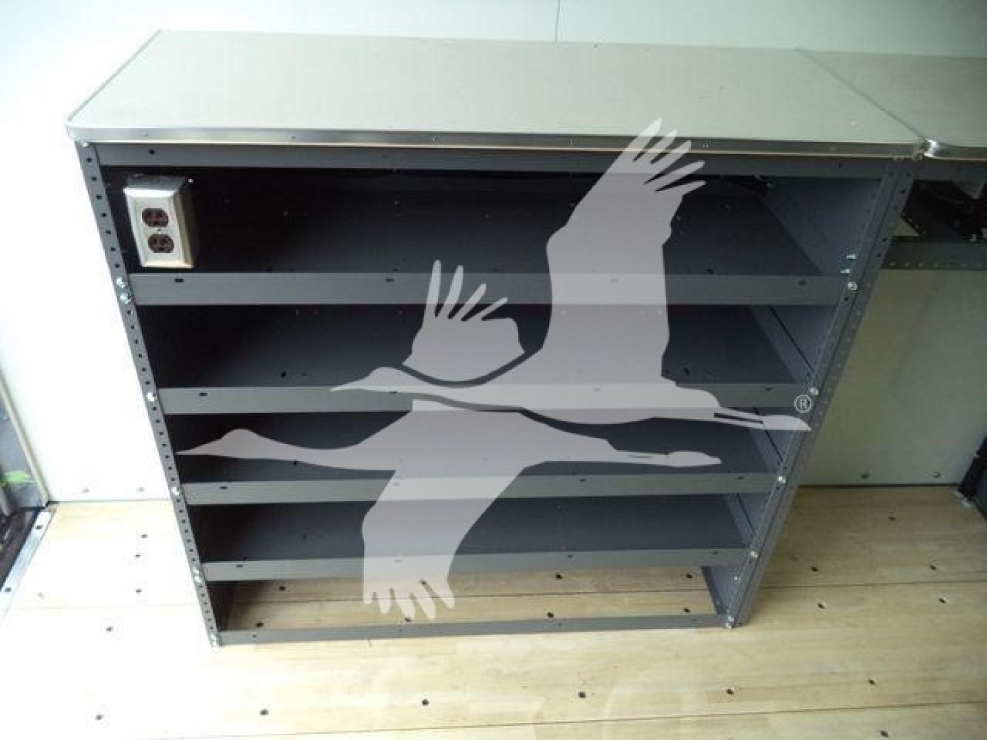 Box truck side service cabinet with three shelves and control box on left, interior wiring panel, on plywood floor.