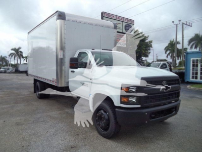 Box truck with a white Chevrolet cab and a large silver box, front grille with Chevrolet bowtie emblem, black bumper; dealership lot in background.