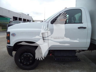 Truck cab side view showing Chevrolet Silverado 6500HD badge on door and white box truck body in a dealership lot.