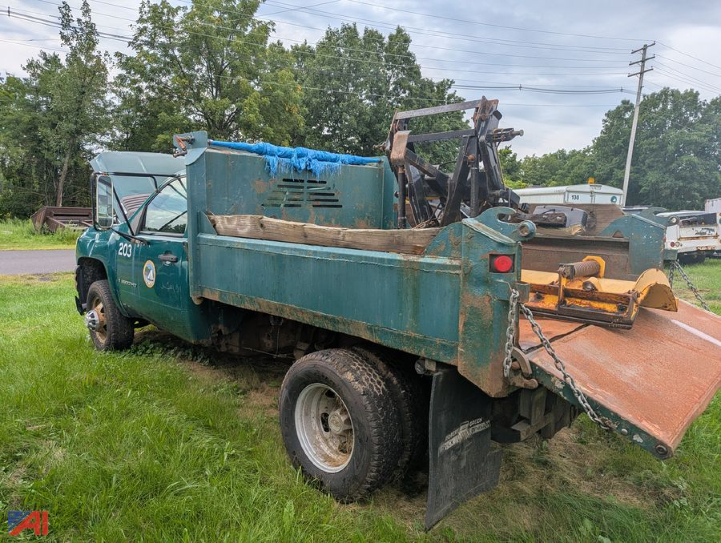 Dump truck with plow attachment showing teal body and flatbed; wheel viewed, back ramp chained.