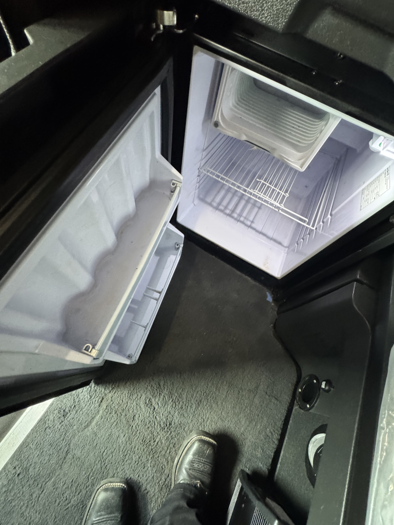 Cabinet and refrigerator area of a Freightliner Cascadia 126 sleeper showing open mini fridge and storage compartments inside the cab.