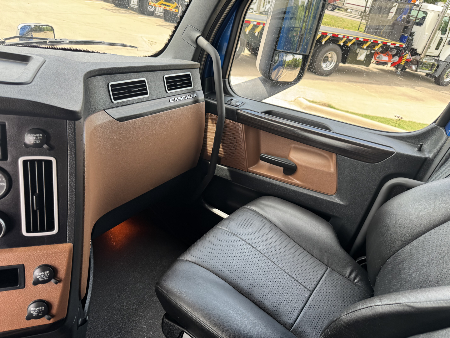 Cab interior of a Freightliner Cascadia 126 truck showing dashboard with brown trim, passenger side door panel, and black leather seat.