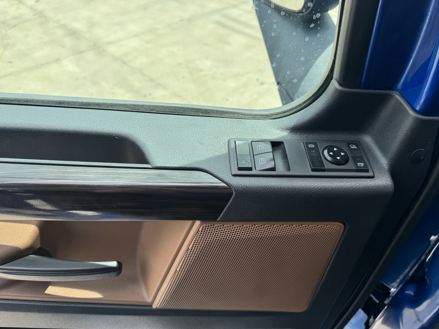 Freightliner Cascadia 126 interior door panel and window controls visible; tan door trim with speaker grille and control buttons on the window switch pad.
