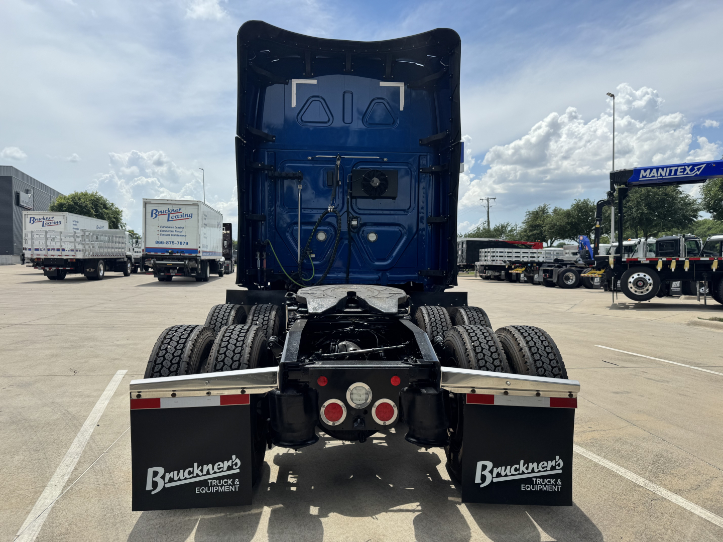 Rear view of a 2022 Freightliner Cascadia 126 in a truck lot showing dual rear axles, black chassis, and mudflaps with BrukeneR text. Visible cables and underbody components.
