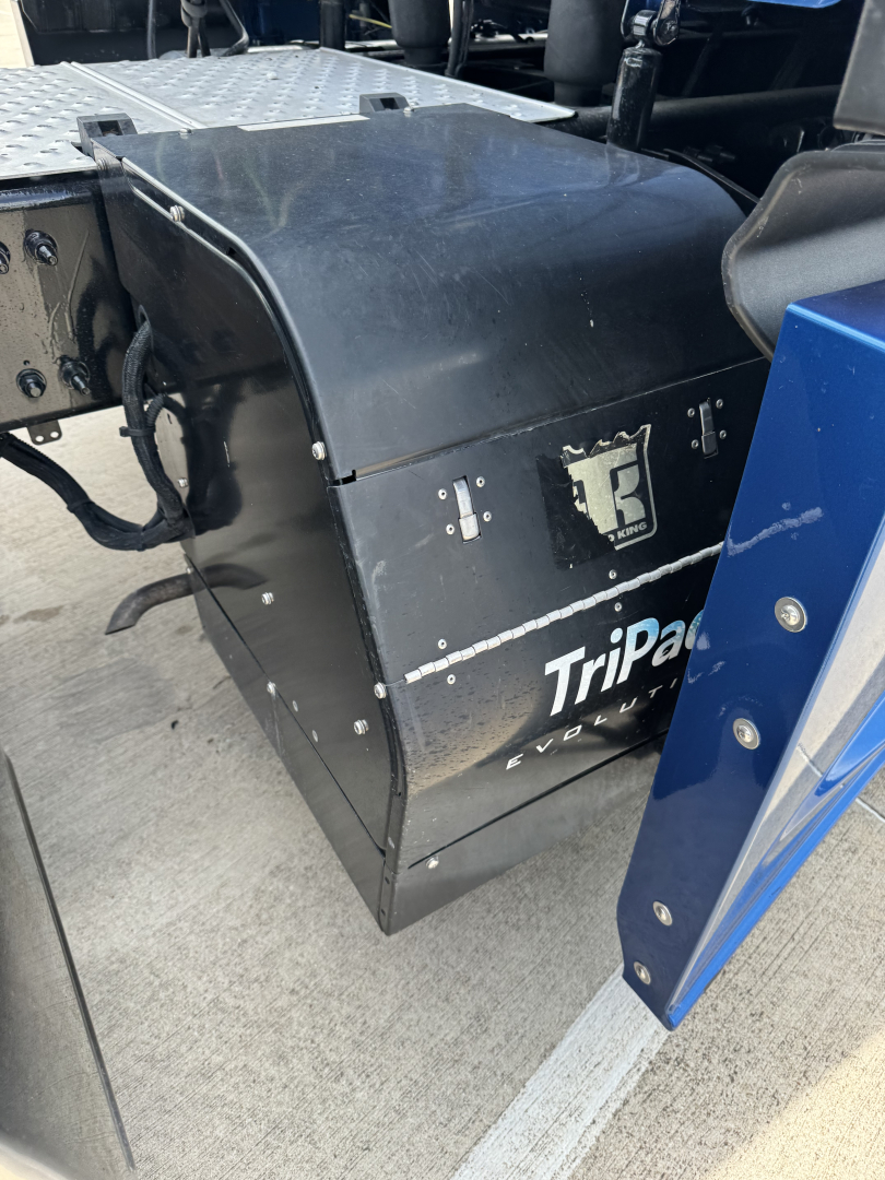 Industrial fuel tank or toolbox mounted on a Freightliner Cascadia truck chassis showing a black metal enclosure with Tripak branding and a small emblem.