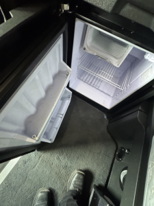 Cabinet and refrigerator area of a Freightliner Cascadia 126 sleeper showing open mini fridge and storage compartments inside the cab.