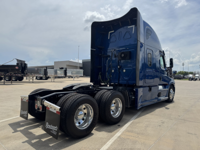 Freightliner Cascadia 126 semi-truck in blue, rear view showing dual rear axles and sleeper cab, no cargo, dealership lot in background.