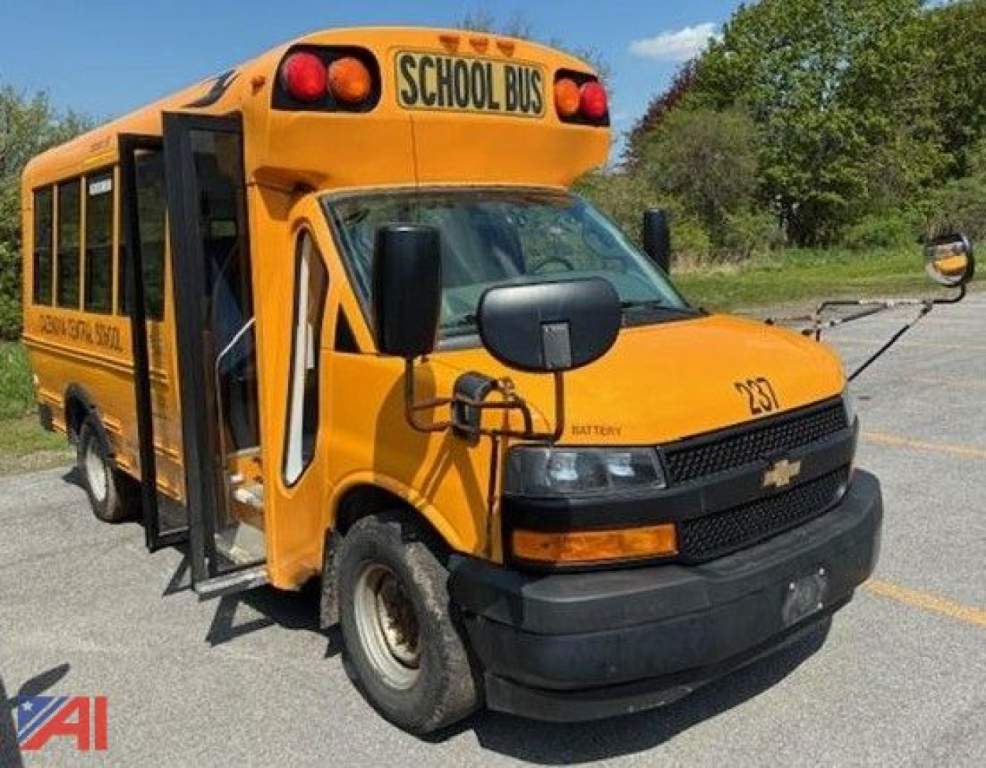 School bus body of a 2018 Chevrolet Express MB2 mini bus in yellow with black front grille, side entry door open, 'SCHOOL BUS' sign on top, and Chevrolet emblem.