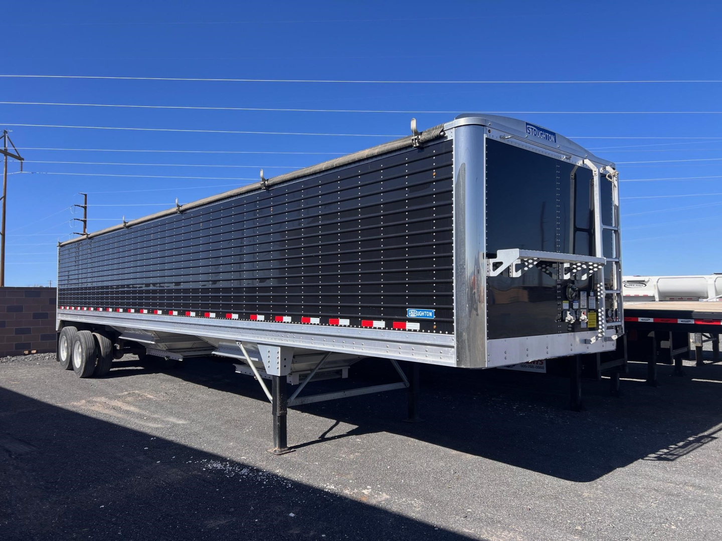 Stoughton grain trailer with black side panels and chrome front posts, triple-axle? No, two-axle with landing gear visible; front corner shows metallic frame and rear unloading area.