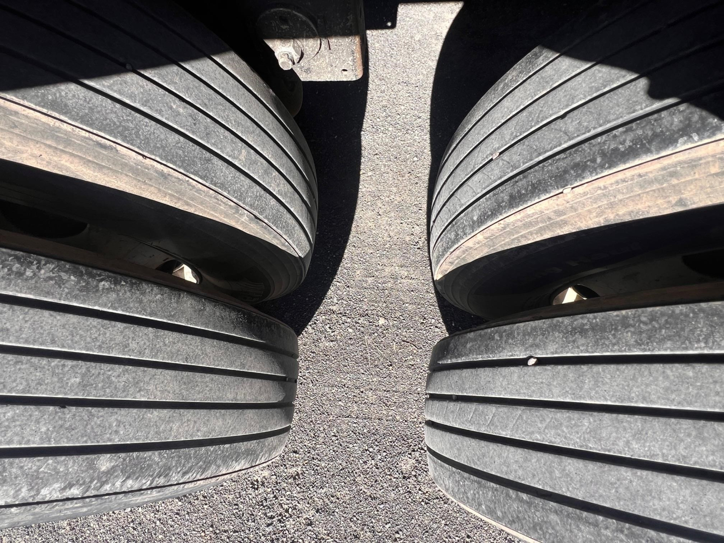 Trailer tire tread close-up showing dual axles and dropped wheel wells with visible road surface.