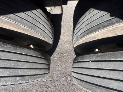 Trailer tire tread close-up showing dual axles and dropped wheel wells with visible road surface.