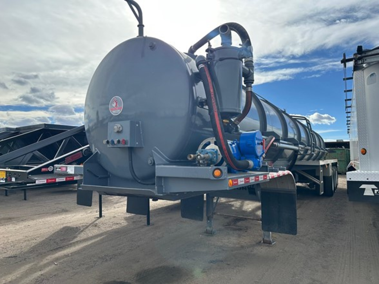 Vacuum tanker trailer in-service rear view showing circular rear tank with hoses and blue pump on right side.