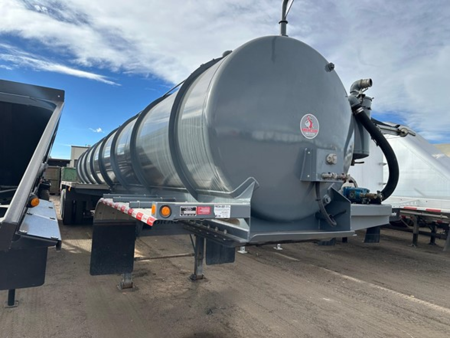 Vacuum tanker trailer showing cylindrical stainless tank and rear access hatch with hoses and support legs.