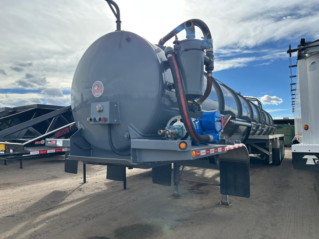 Tank trailer with a large cylindrical vacuum tanker and blue piping, rear view showing support legs and mounting brackets.