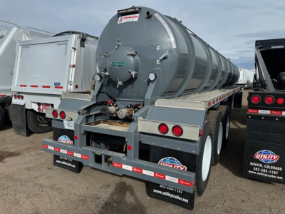 Vacuum tanker trailer with grey cylindrical tank and rear access hatch, mounted on a triple-axle trailer with white wheels; Dragon logo and various stickers visible on rear.