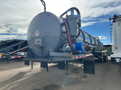 Tank trailer with a large cylindrical vacuum tanker and blue piping, rear view showing support legs and mounting brackets.