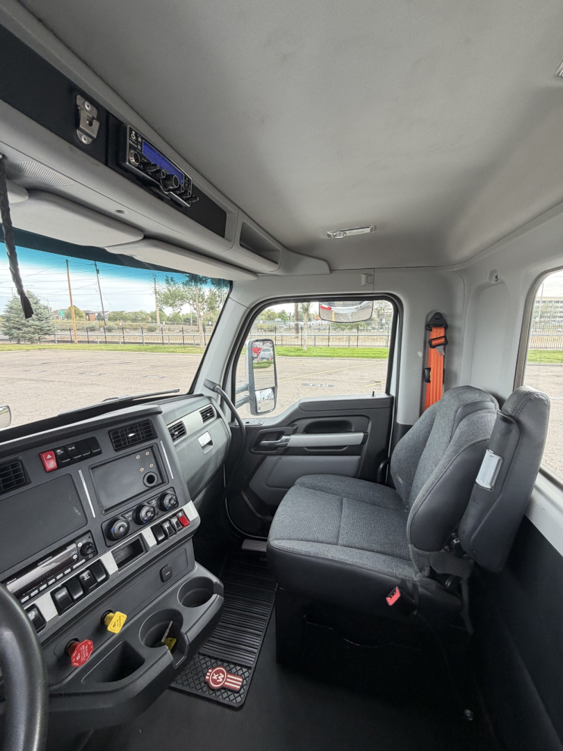 Inside view of a Kenworth T880 cab showing steering wheel, dashboard with controls, and two front seats in a daycab configuration.