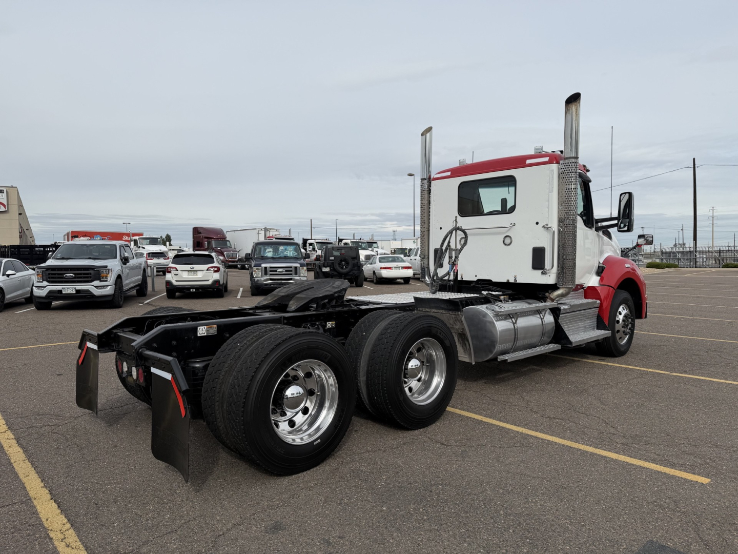 Kenworth T880 conventional daycab tractor in a parking lot, rear view showing dual rear axles and frame, red and white cab, chrome fuel tanks, no trailer attached.