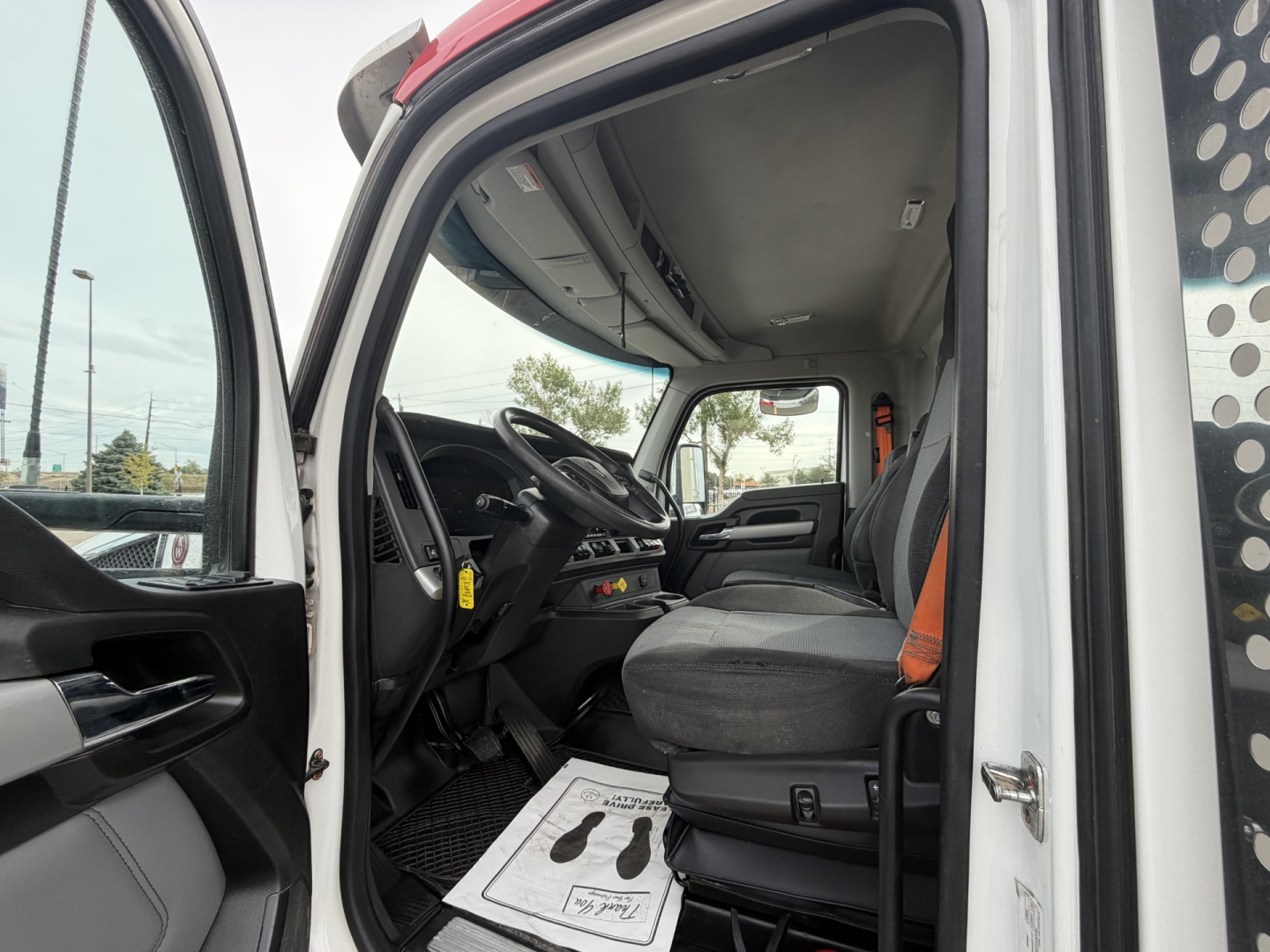 Kenworth T880 truck cab interior showing driver seat and dashboard from open door, with steering wheel and controls visible.