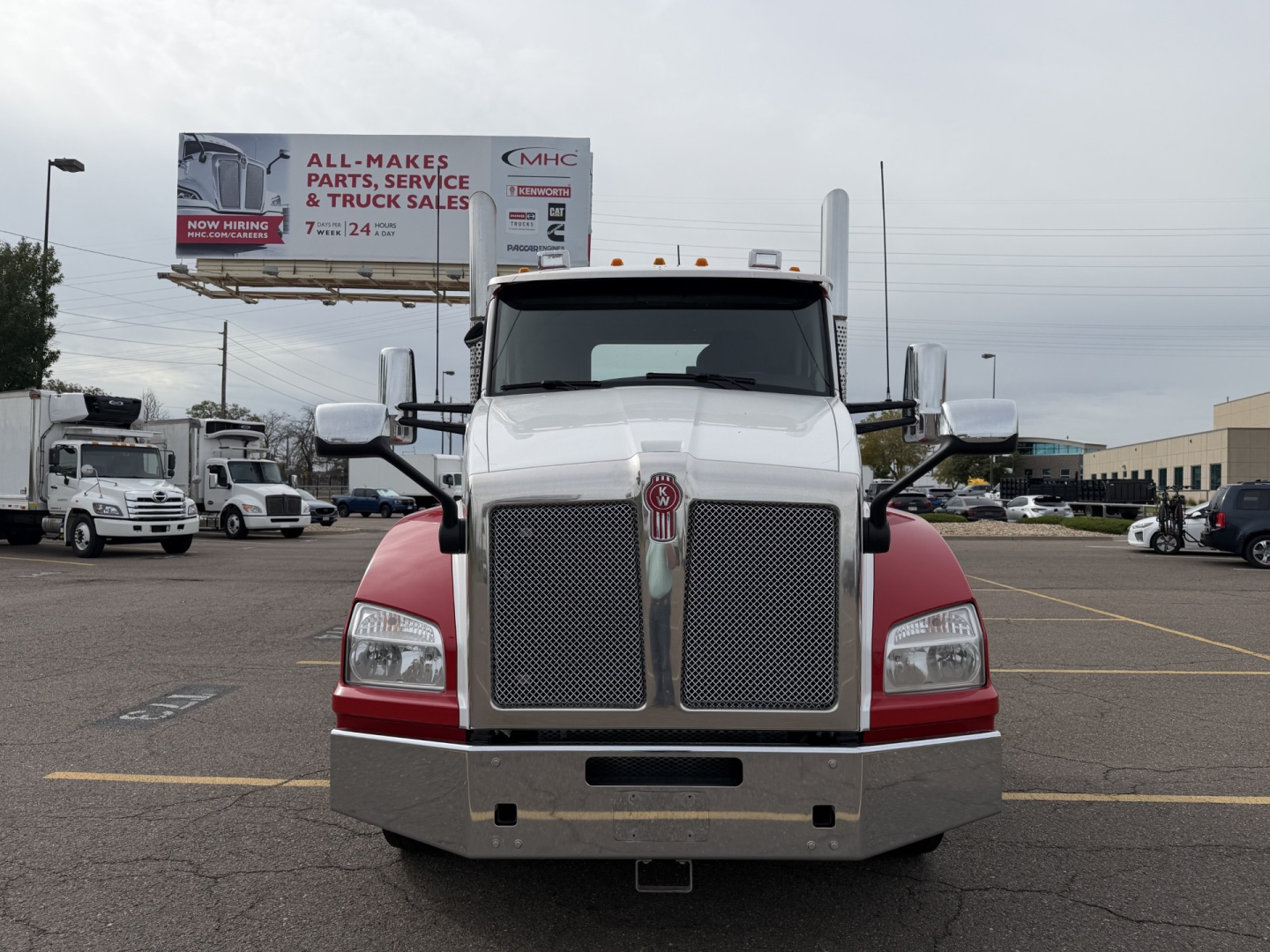Kenworth T880 conventional daycab front view showing large chrome grille, dual headlights, white cab with red lower panels, and bumper.