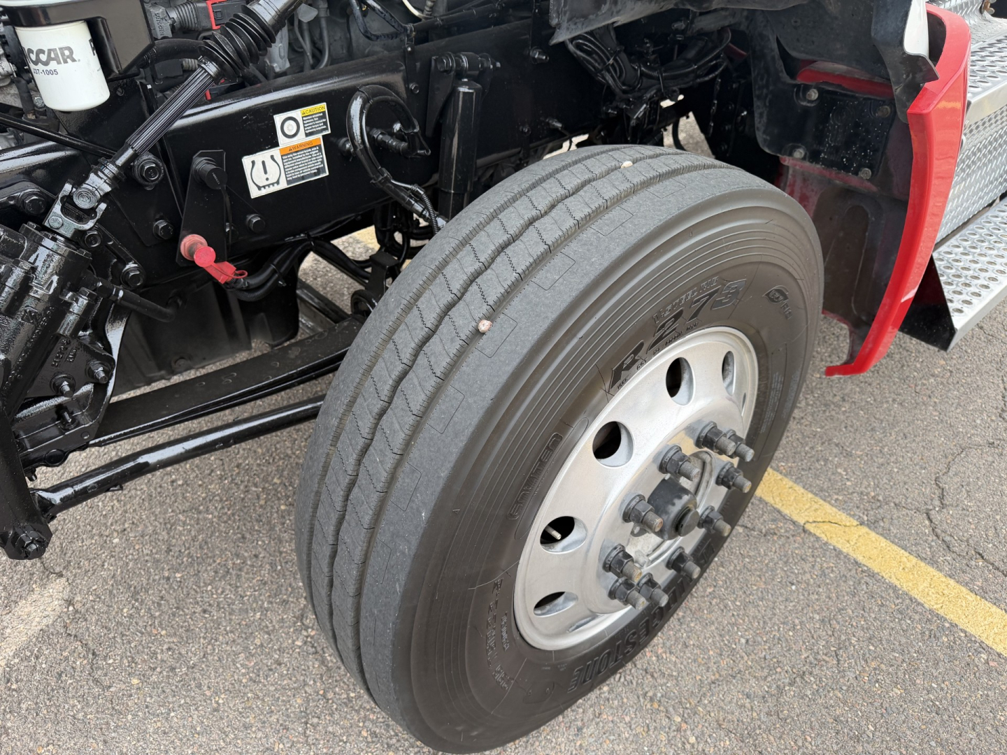 Kenworth T880 front wheel assembly and chassis with tire, visible labels, and hydraulic components.