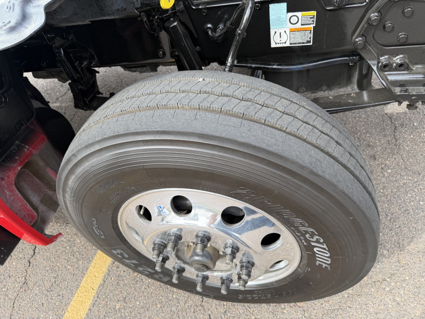 Kenworth T880 front wheel and tire assembly showing Goodyear tire and chrome wheel with lug nuts; undercarriage components and frame visible.