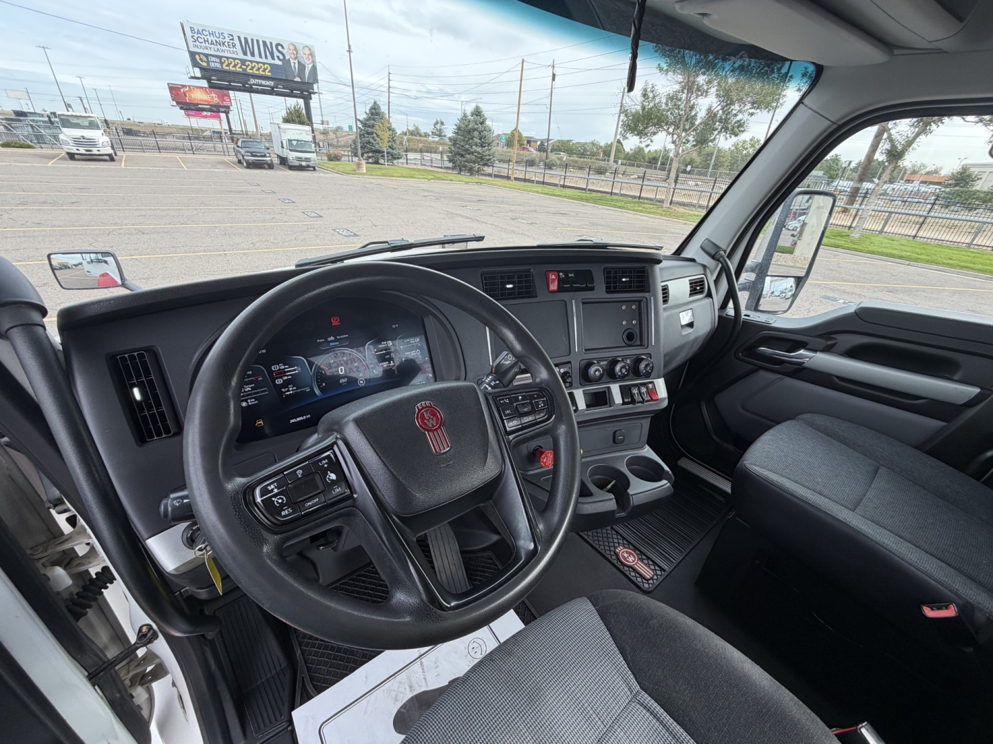Interior of a Kenworth T880 cab showing steering wheel with KW logo, dashboard with digital gauges, center console, and driver seat. Visible exterior rearview mirrors and windshield.