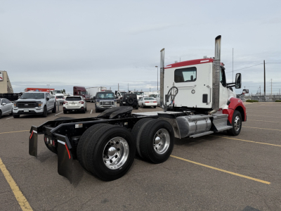 Kenworth T880 conventional daycab tractor in a parking lot, rear view showing dual rear axles and frame, red and white cab, chrome fuel tanks, no trailer attached.