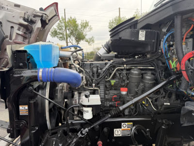 Kenworth T880 engine bay showing blue coolant reservoir, air filter canister, hoses, wiring looms, and various engine components.