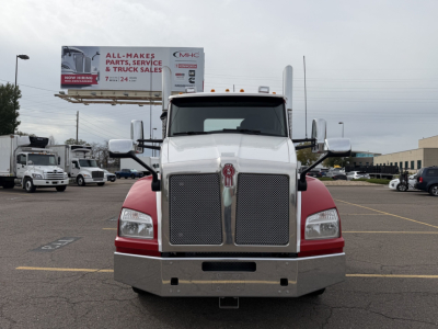 Kenworth T880 conventional daycab front view showing large chrome grille, dual headlights, white cab with red lower panels, and bumper.