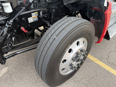 Kenworth T880 front wheel assembly and chassis with tire, visible labels, and hydraulic components.