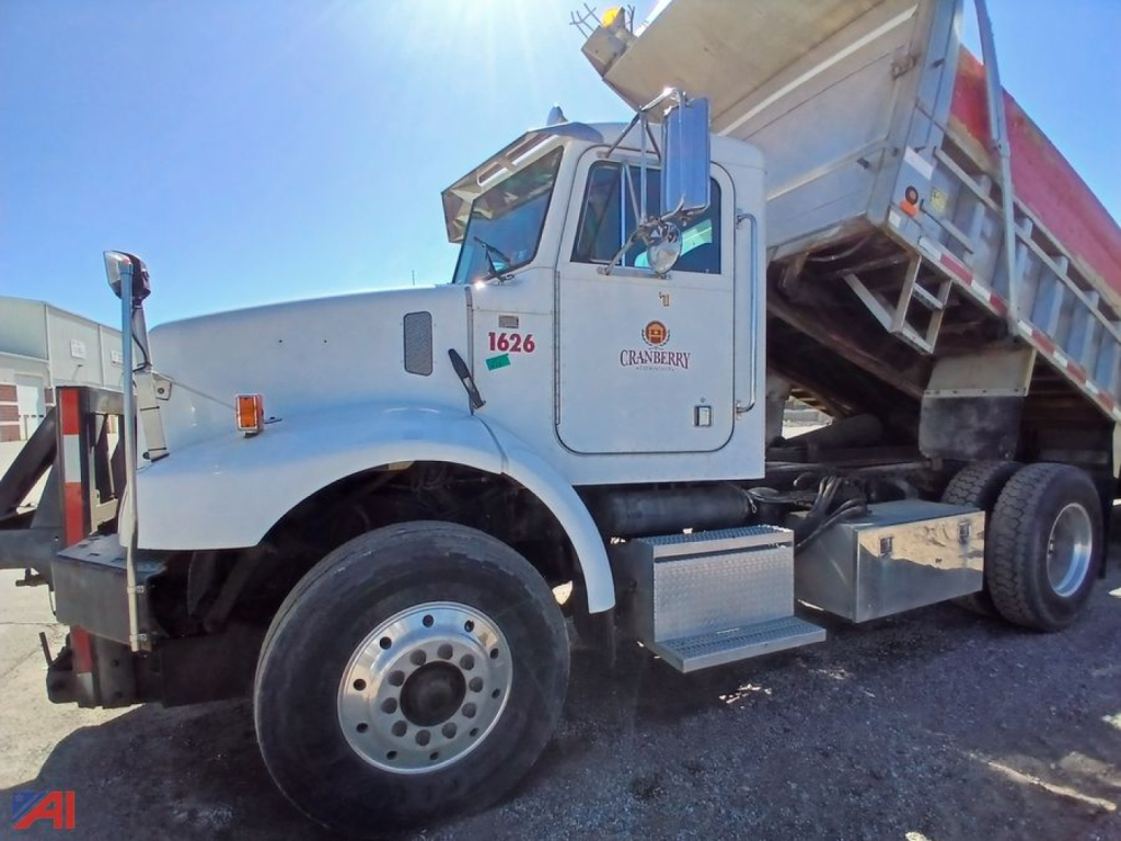 Peterbilt 330 dump truck side view showing cab, dump bed raised, front wheel and operator door with numbers and decals.