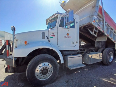 Peterbilt 330 dump truck side view showing cab, dump bed raised, front wheel and operator door with numbers and decals.