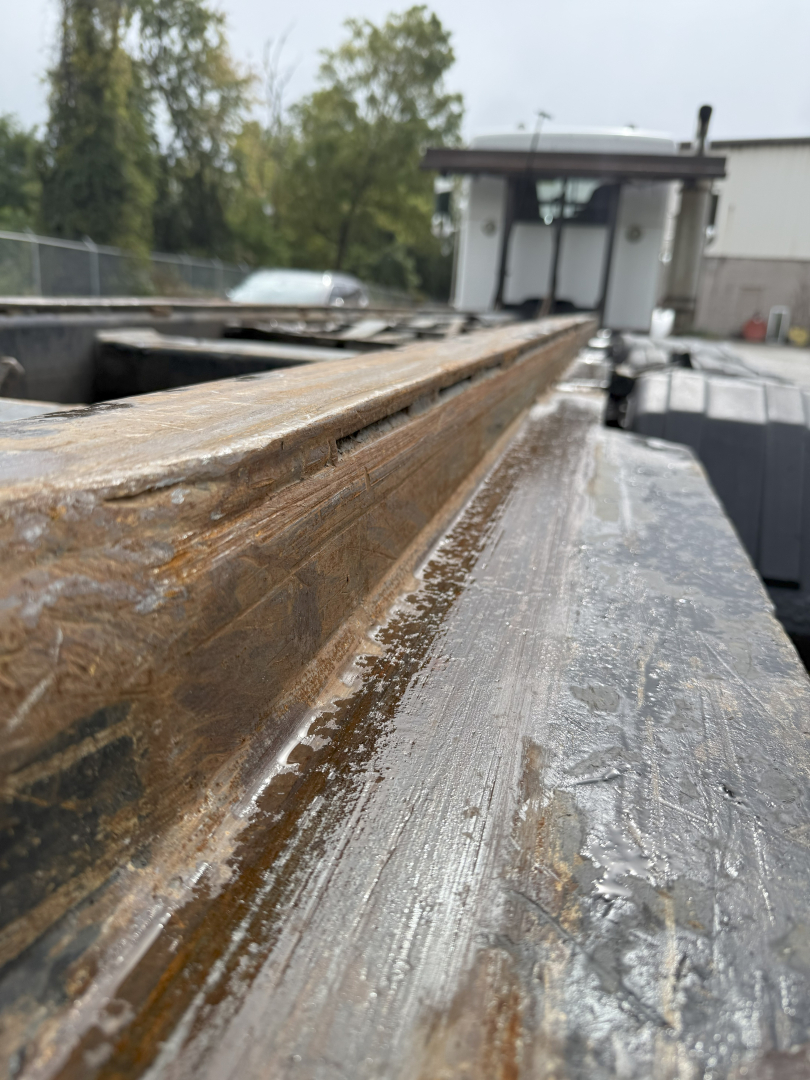 Forklift bed edge of a 2003 Kenworth T800 roll-off truck showing rust and metal surface with a control cab in background.