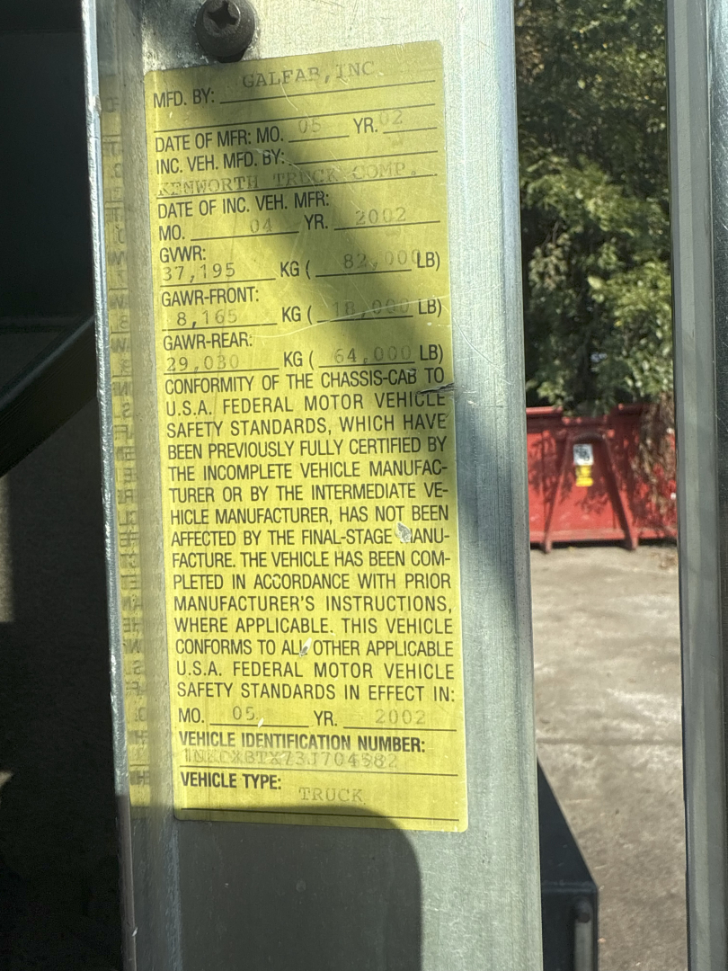 Label on vehicle window showing manufacturer and GAWR/ GVWR information for a Kenworth T800 rolloff truck.