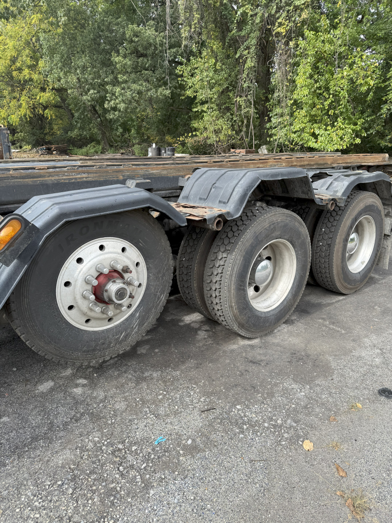 Three rear axles of a Kenworth T800 roll-off truck with black fenders and worn tires; visible wheels and rims, some rust on hub area, flatbed/frame in background.