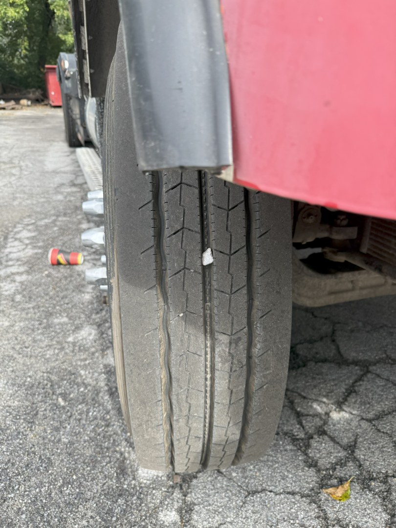 Truck wheel/view of tandem rear tires on a 2003 Kenworth T800 roll-off truck showing tread pattern and side of red fender.