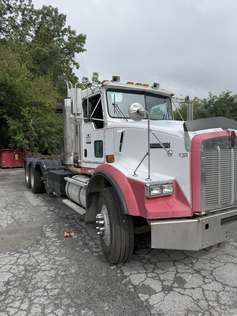 Kenworth T800 roll-off truck in-service showing side cab with chrome exhaust stacks and pink fenders, front grille, dual rear axles, VIN visible in listing