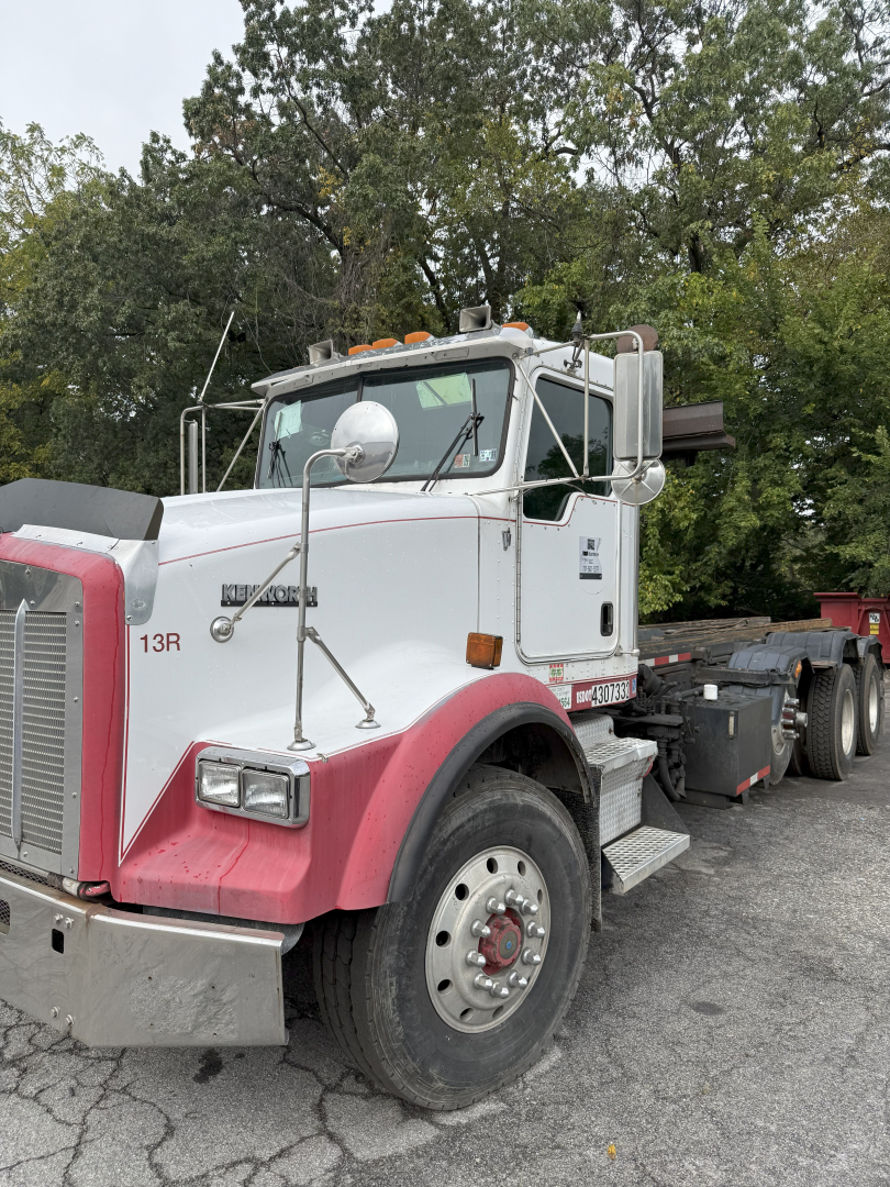 Kenworth T800 rolloff truck side view showing white cab with pink fenders and chrome mirrors.