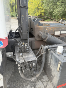 Kenworth T800 rolloff truck showing hydraulic lines and control valves near the crane base with hoses and metal fittings.