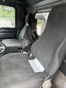 Cab interior of a 2003 Kenworth T800 with two front seats and a folded jacket hanging near the window.