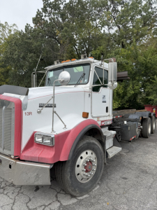 Kenworth T800 rolloff truck side view showing white cab with pink fenders and chrome mirrors.