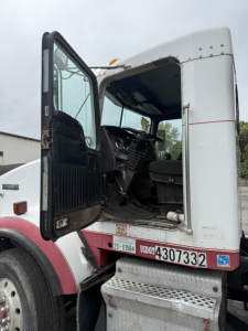 Kenworth T800 truck cab with door open showing interior steering wheel and dashboard, rolloff truck configuration, side step with metal stairs and VIN plate visible.