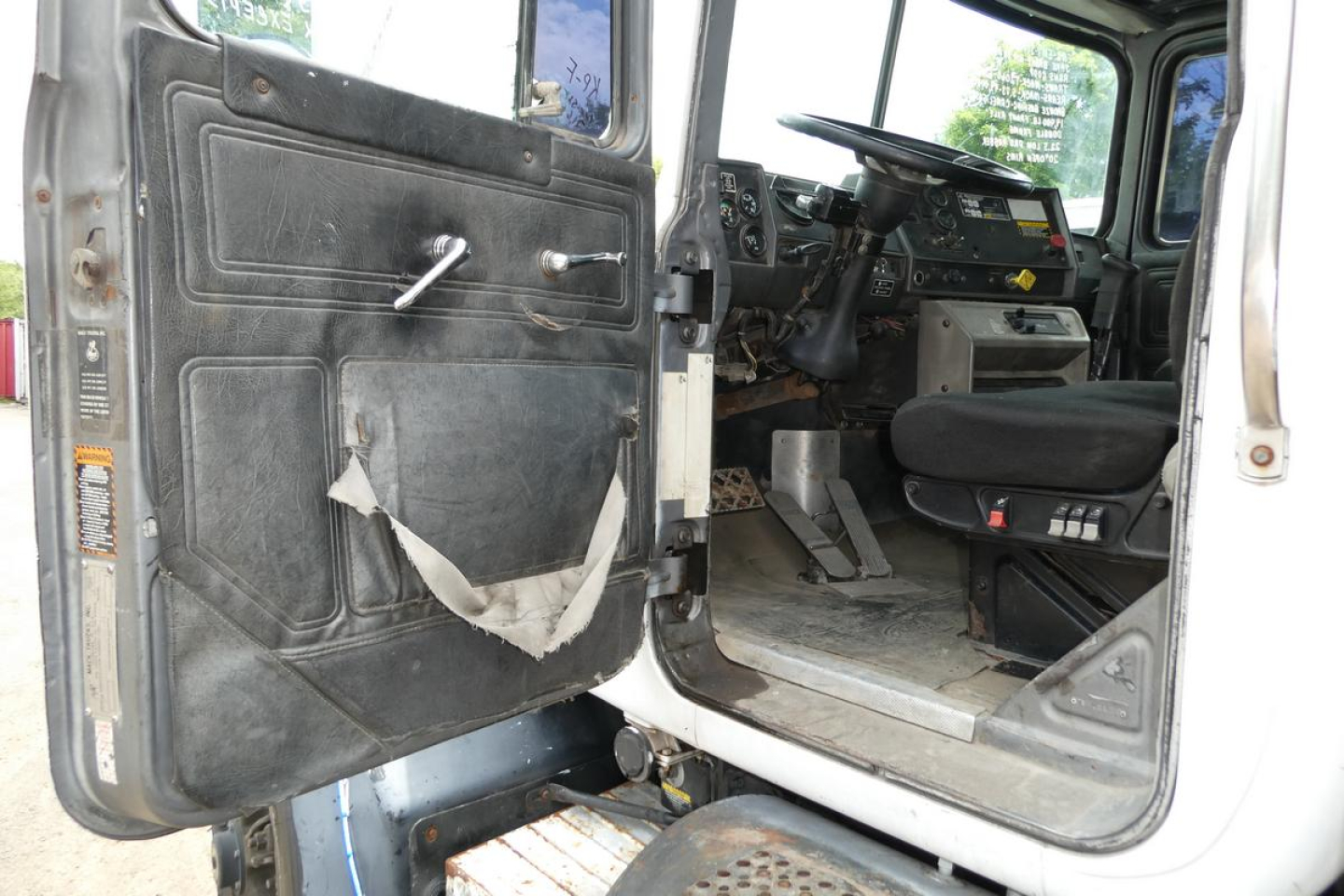 Truck cab interior view of a 1997 Mack RD690S showing open driver door, steering wheel, dashboard, and worn door panel with torn fabric.